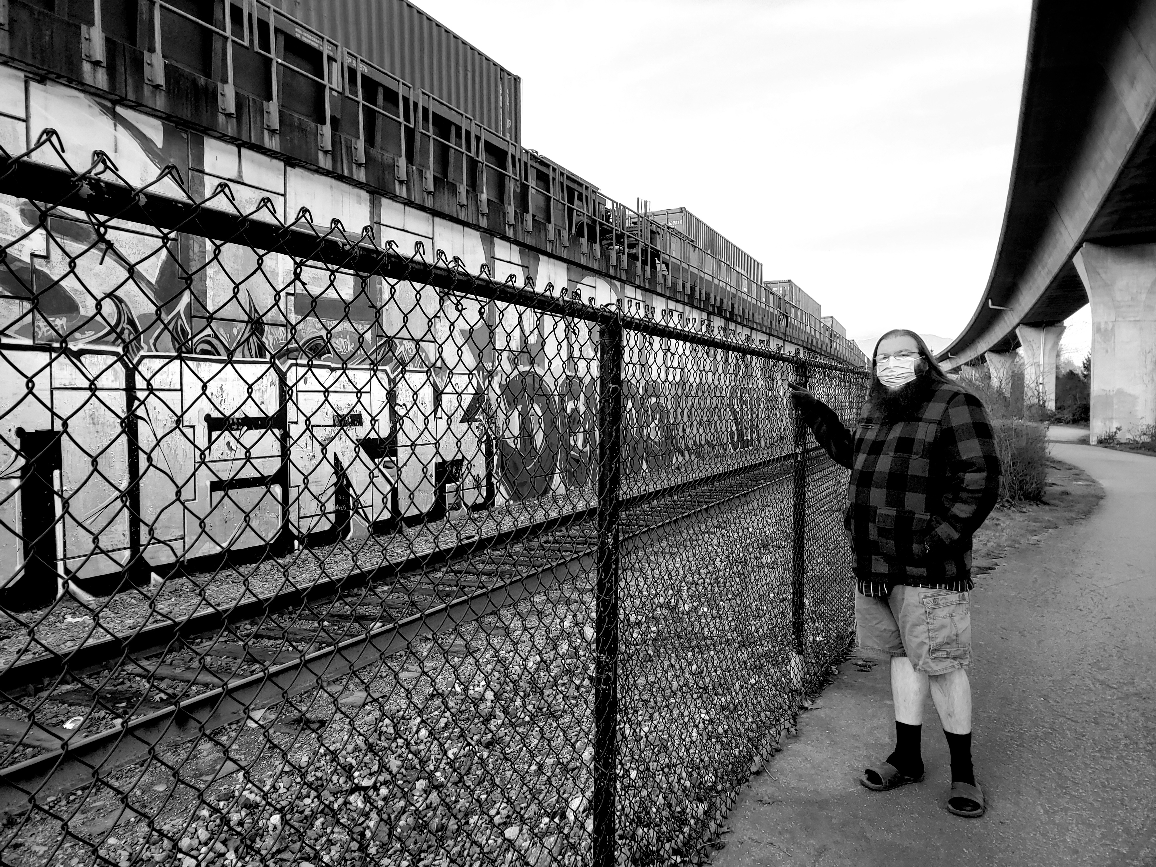 Black and white photograph of graffiti along train tracks with man by B.Y. Penman